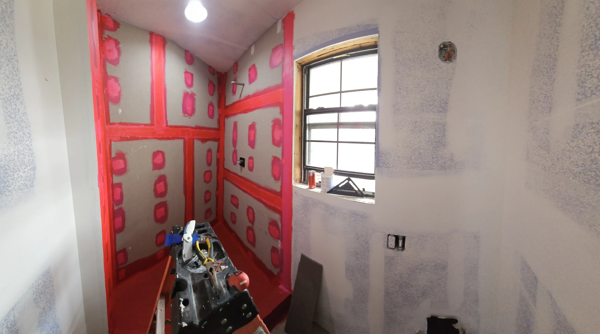 Red waterproofing membrane applied over the shower walls before tile.