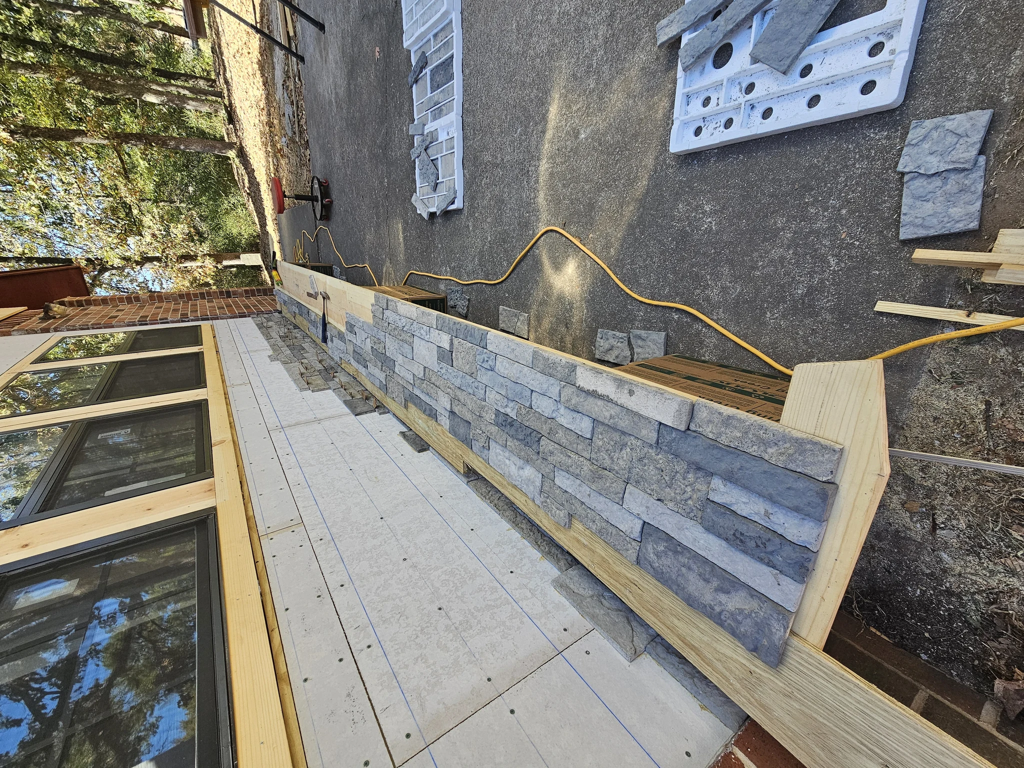 Stone veneer coursing rising up the wall with stone laid out ready.