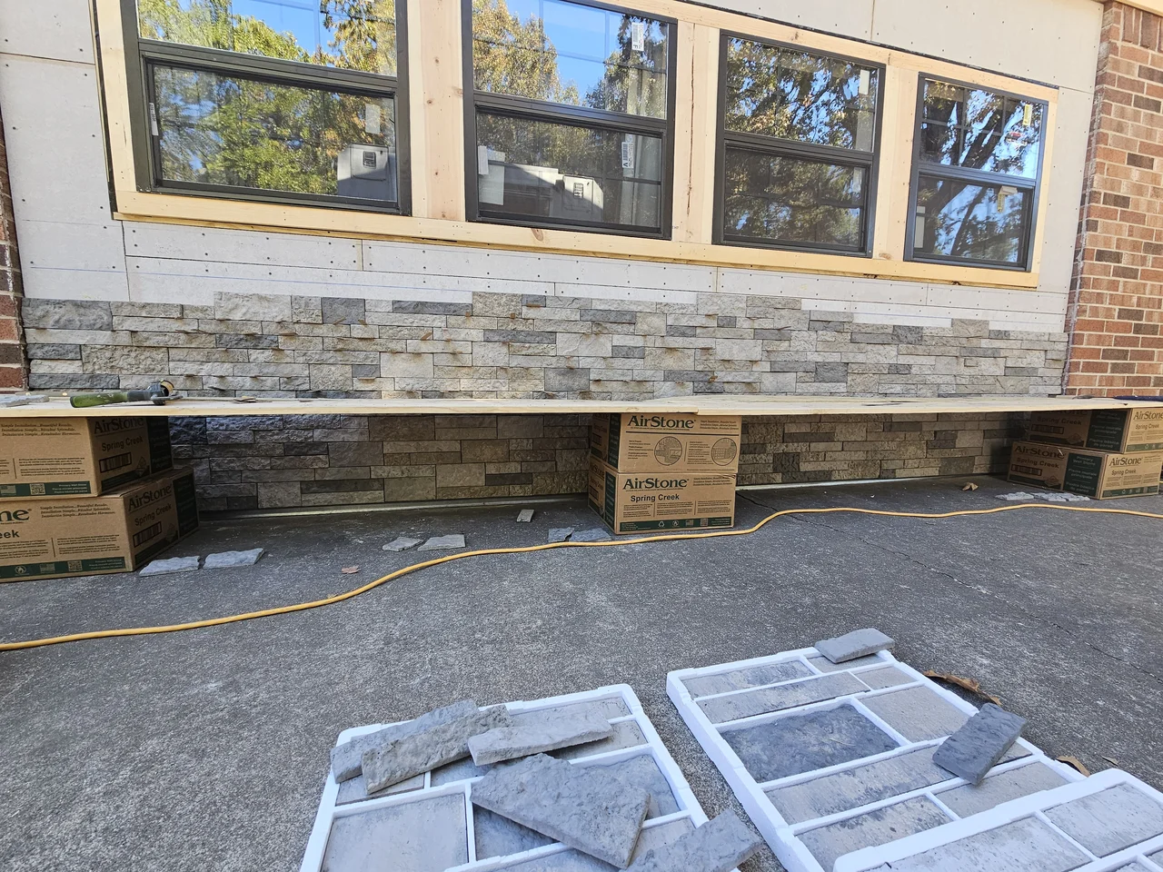 Stone veneer progress with cut stone staged across the driveway.