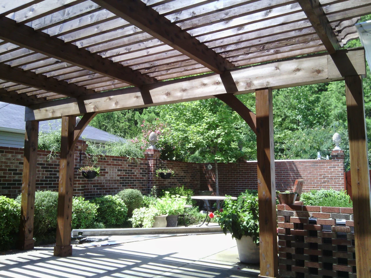 A raking view down the length of the pergola rafters in dappled light.