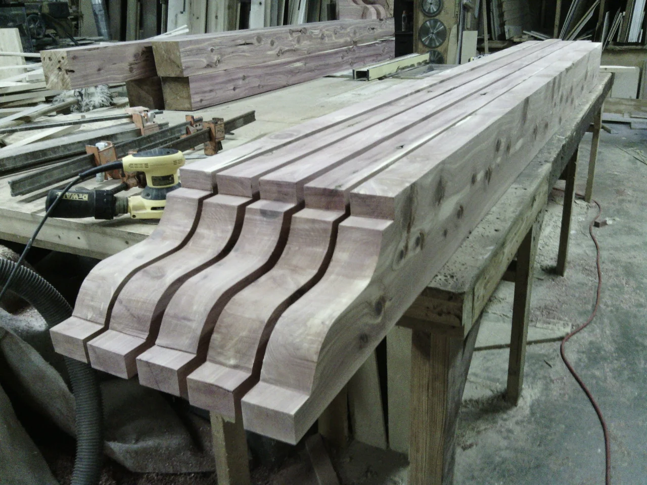 A rank of shaped ogee rafter tails laid out together on the shop bench.